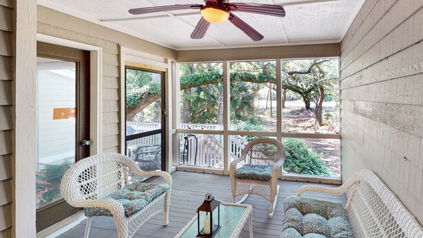 A covered porch with wicker furniture, a ceiling fan, and a view of trees and a fence.