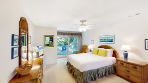 Un dormitorio con cama, ventilador de techo, cómoda, espejo y ventana con vistas al exterior.