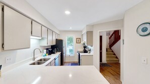 A modern kitchen with white cabinets, stainless steel appliances, and a wooden floor.