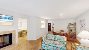 Una sala de estar con chimenea, un sofá, un comedor y un televisor mostrando 'SLAND REALTY'.