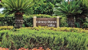 A sign for Fairway Dunes Villas surrounded by lush greenery and ornamental plants.