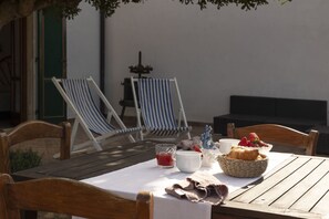 A wooden table with a white tablecloth, two striped lounge chairs, a wicker basket with pastries, a white mug, and a glass of red drink.