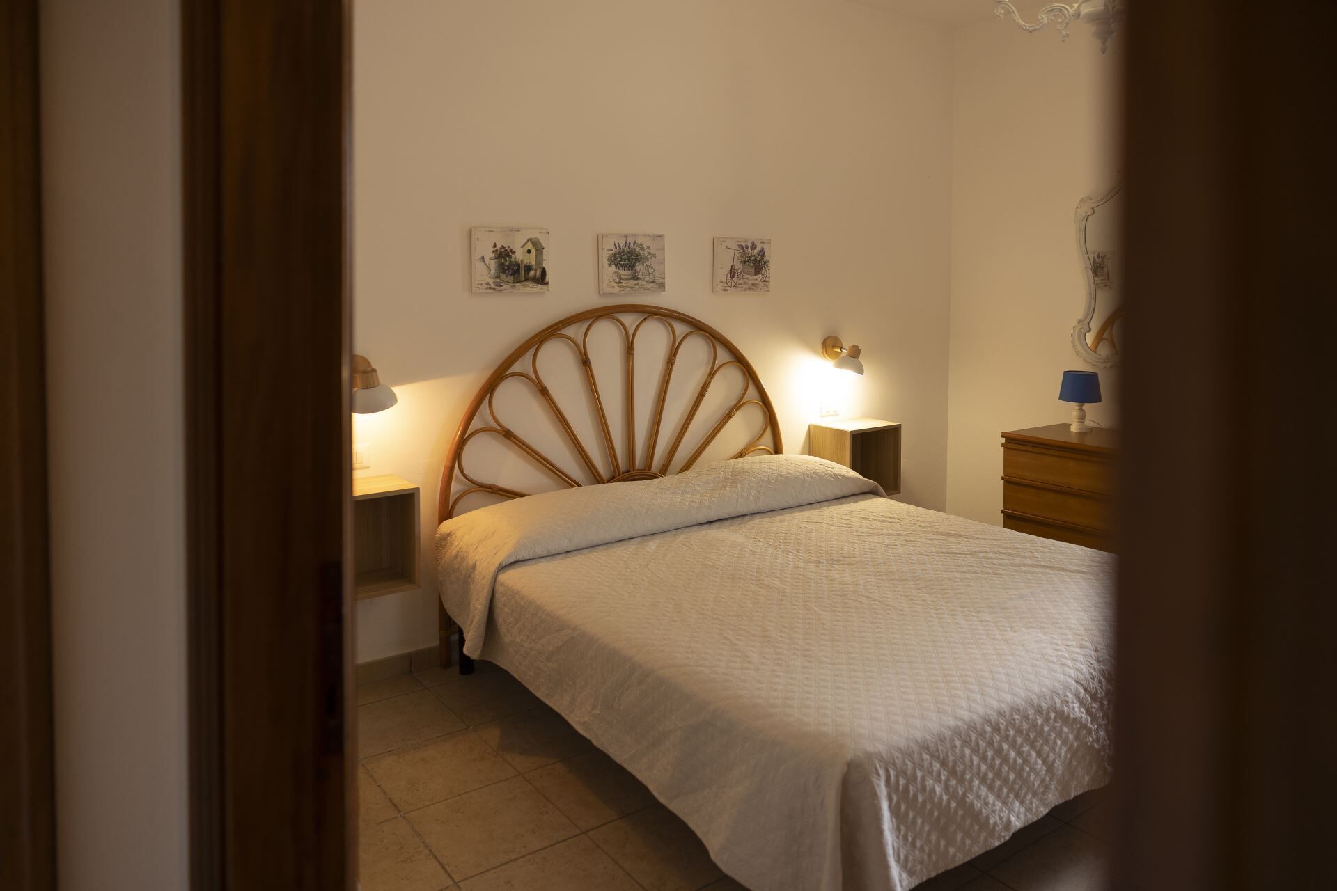 A bedroom with a bed, two bedside lamps, a dresser, and three wall-mounted pictures.
