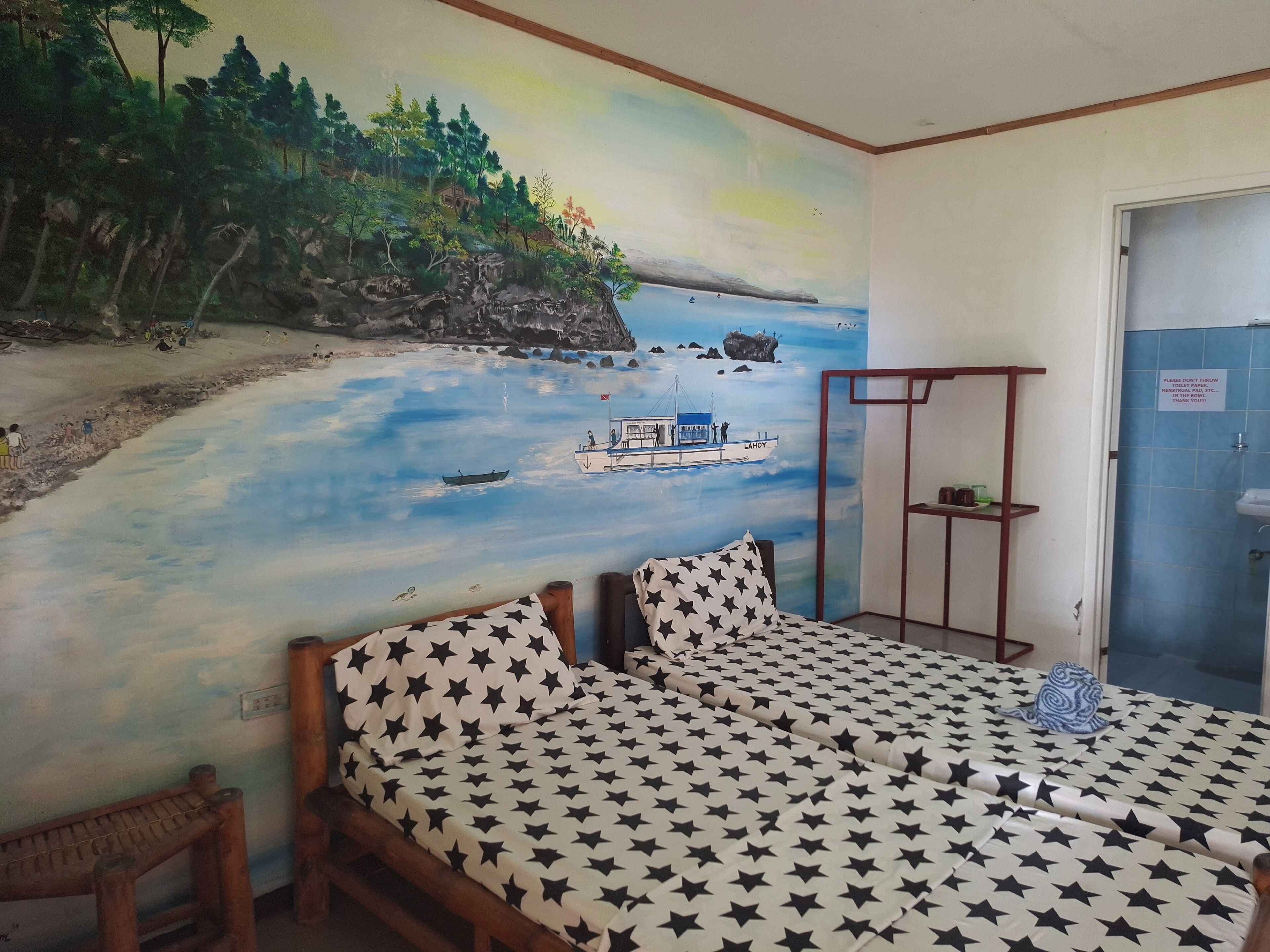 A room with a mural of a beach scene, a bed with a star-patterned bedspread, and a wooden bench.