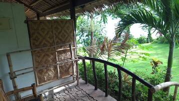 A covered outdoor area with a bamboo railing, a woven wall, and a view of a lush garden.