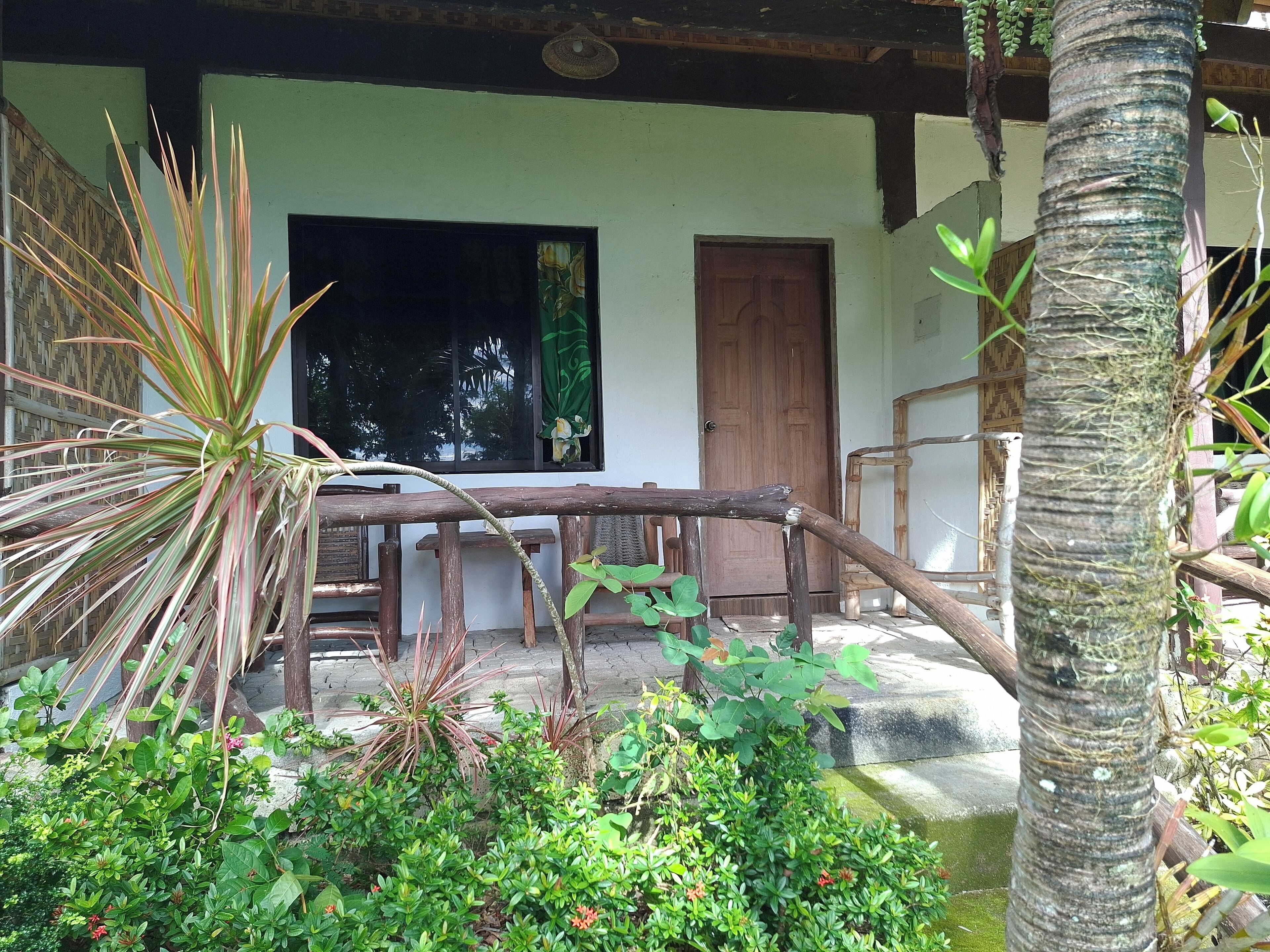 A wooden porch with a bench, a wooden door, and a window with a green curtain.