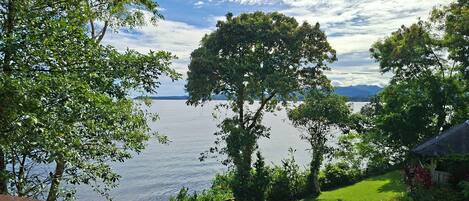 Une vue depuis un espace extérieur abrité, donnant sur un lac bordé d’arbres et d’une zone herbeuse.