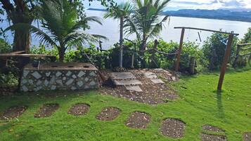 A garden with a stone bench, a small pond, and a view of a lake.