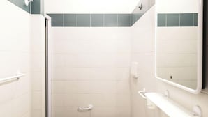 A bathroom with white tiles, a shower, a sink, and a mirror.