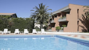 A swimming pool with lounge chairs, a palm tree, and a building with balconies.