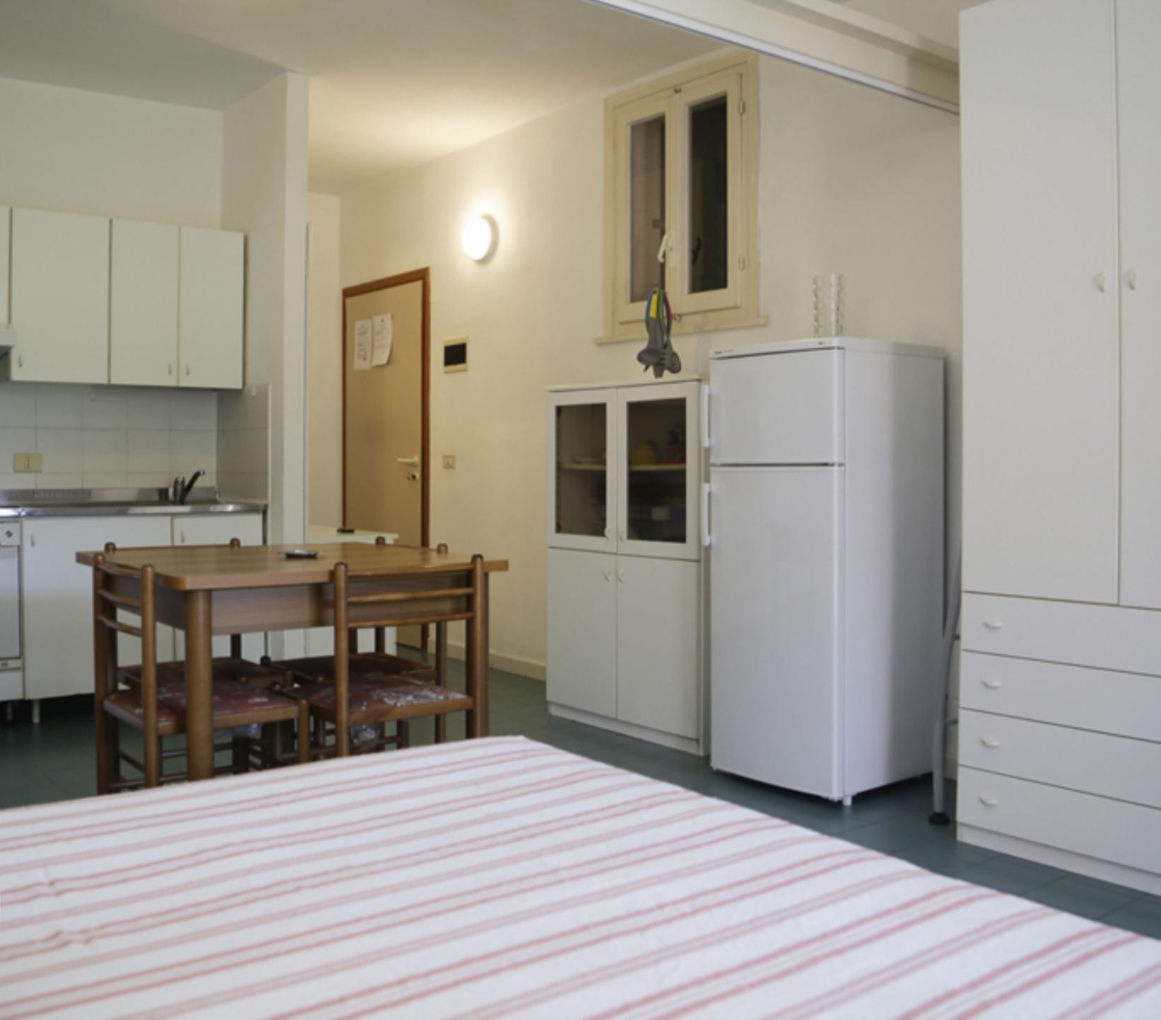 A compact kitchen with white cabinets, a wooden dining table, and a refrigerator.