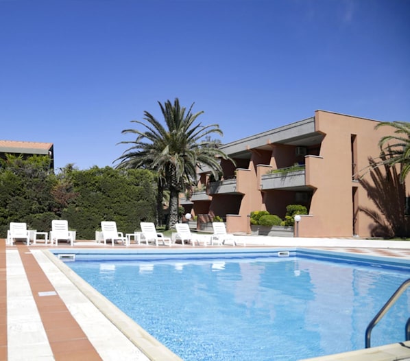 Una piscina con sillones blancos y un edificio con balcones.
