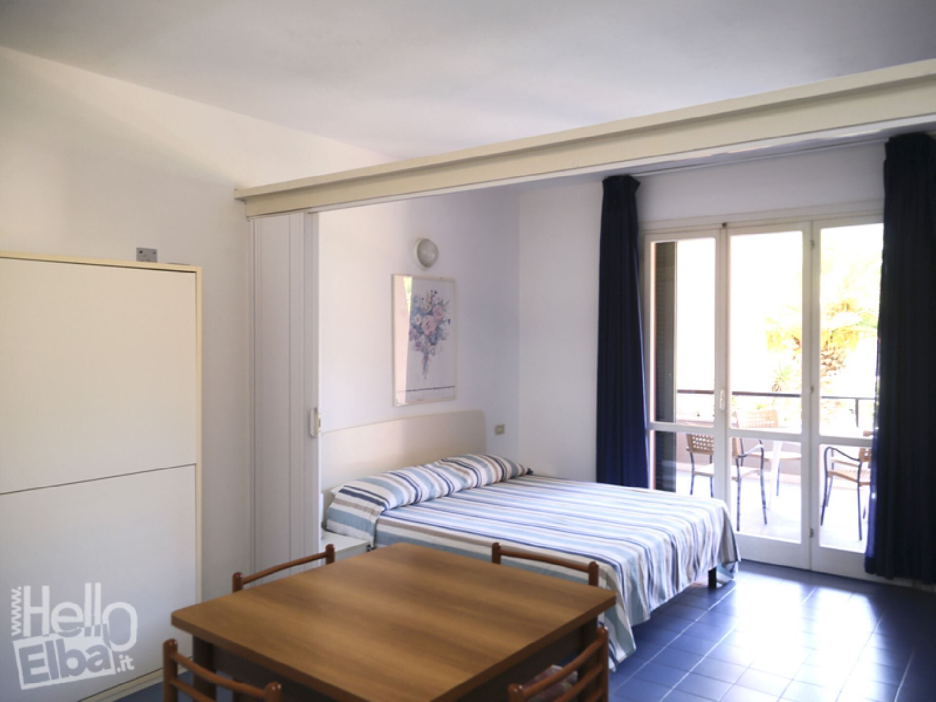 Een slaapkamer met een bed, een houten tafel en een raam met gordijnen.