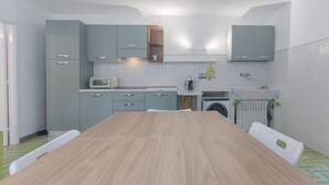 A modern kitchen with grey cabinets, a wooden table, a built-in oven, and a washing machine.