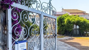 A wrought iron gate with a sign, a cobblestone path, and a building with a tiled roof in the background.