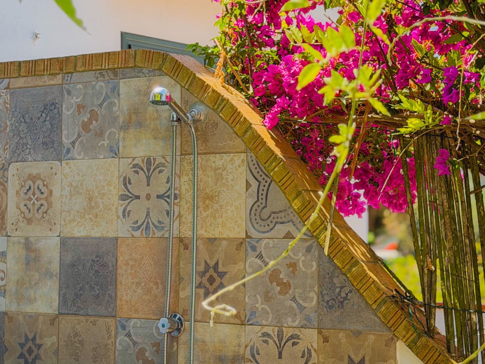 A tiled wall with a showerhead, a decorative metal fence, and vibrant pink bougainvillea flowers.