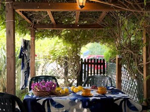 An outdoor dining area with a table set for two, surrounded by greenery and a wooden pergola. - Located on the ground floor, it consists of a living room with kitchenette and sofa bed, a double be (Portoferraio)