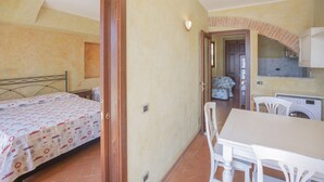 A small, well-lit room with a bed, a table, and a chair. There is a door leading to another room with a table and chairs. - Tastefully furnished, it consists of a family room with a double bed and a single bed, a small livin (Portoferraio)