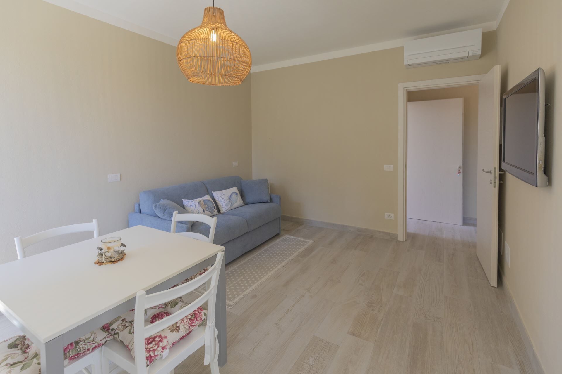 Une petite pièce bien éclairée, avec une table et des chaises blanches, un canapé bleu et un luminaire suspendu.
