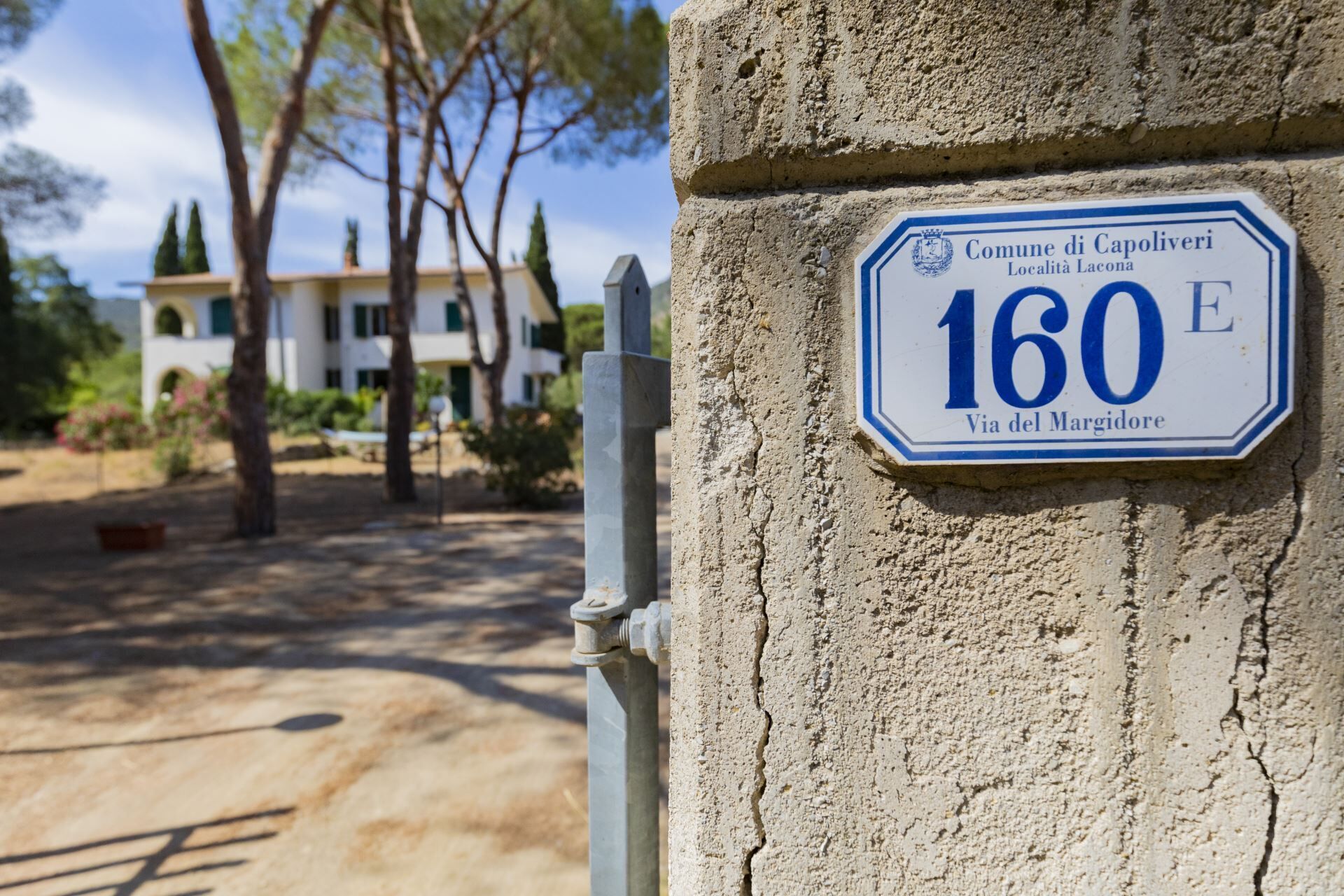 A sign with the number 160 E, indicating a street address in Comune di Capoliveri, Località Lacona.