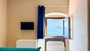Ein Zimmer mit einem Bett, einem Flachbildfernseher, einem Drucker und einem Fenster mit Blick auf Berge und Wasser.
