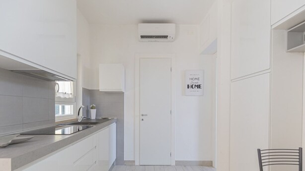 A modern kitchen with white cabinetry, a stainless steel sink, and an air conditioning unit above the door.