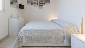 A bedroom with a bed, a dresser, a TV mounted on the wall, and a series of framed pictures above the bed.