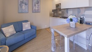 Eine moderne Küche mit weißen Schränken, einem blauen Sofa und einem Essbereich mit Holztisch und -stühlen.