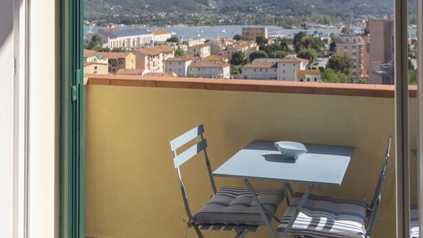 Ein Balkon mit Tisch und zwei Stühlen, mit Blick auf eine Stadt und Berge.