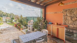 An outdoor patio with a stone floor, a table with a patterned tablecloth, wicker chairs, a built-in kitchen with a stone wall, and a hanging pendant light. - A short distance from the center of Rio Marina, easily reachable on foot, we offer our clients a cha (Rio Marina)