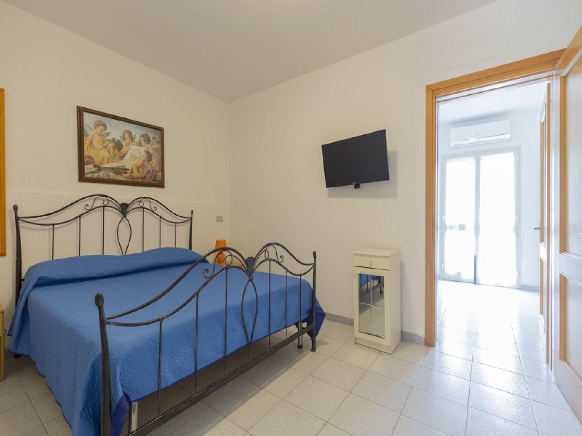 A bedroom with a bed, a painting, a television, and a door leading to another room.
