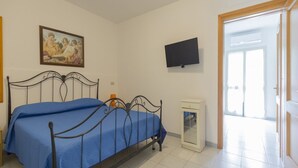 A bedroom with a bed, a painting, a television, and a door leading to another room.