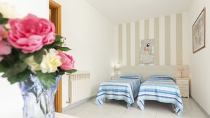 A bedroom with two beds, a radiator, a bedside table with a lamp, and a framed picture on the wall.