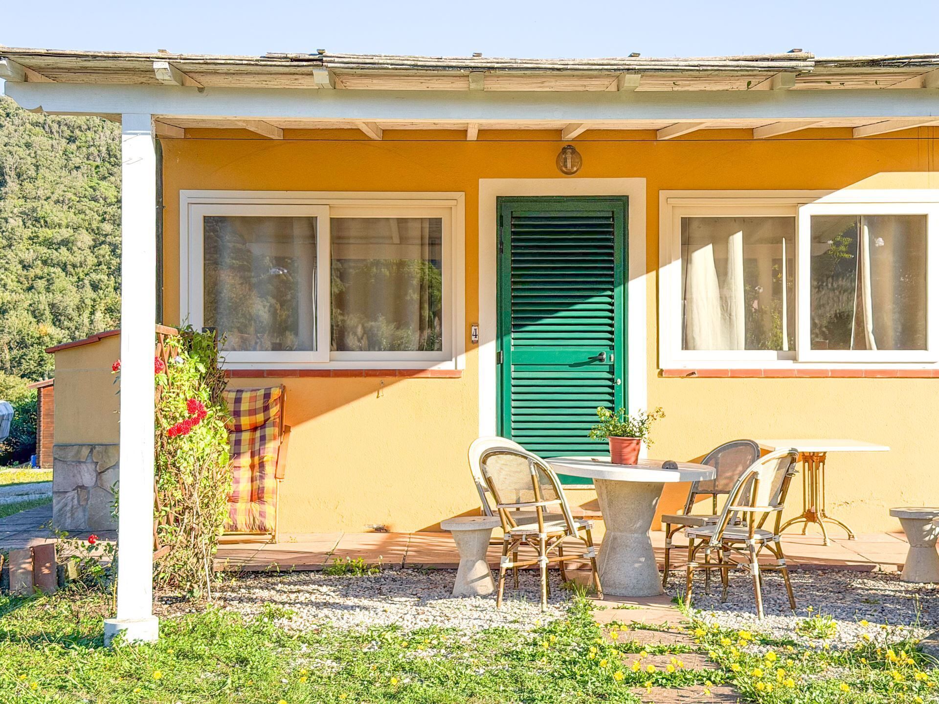 Un edificio amarillo con puerta verde, dos ventanas y un patio con sillas y una mesa.