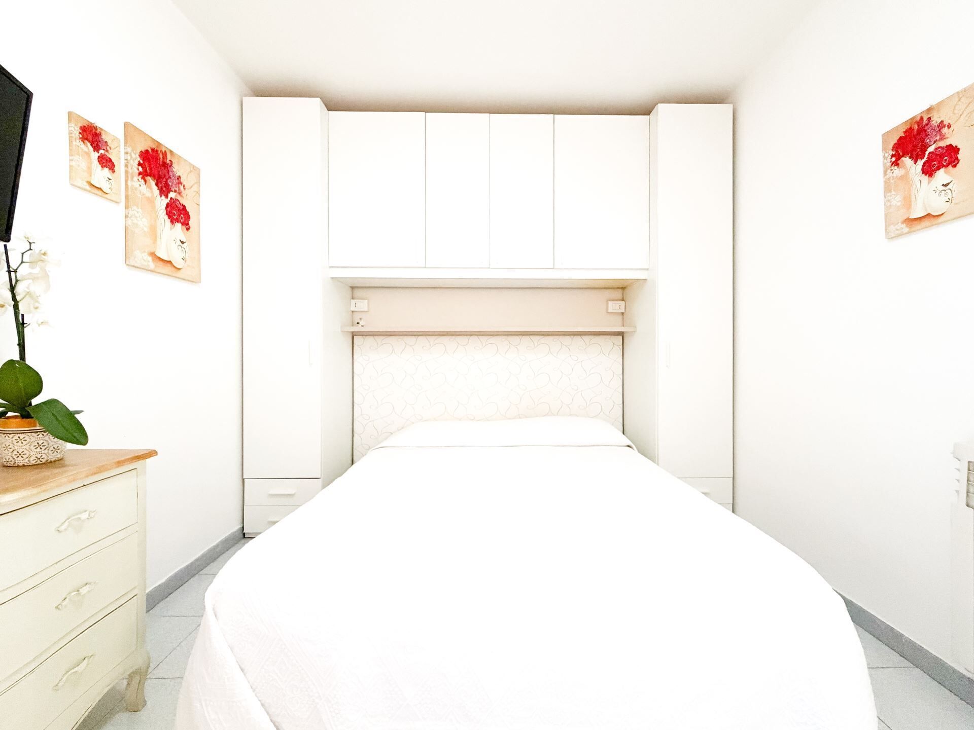 Ein Schlafzimmer mit einem Bett, einem Schminktisch, einem Fernseher und Bildern an den Wänden.