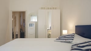 Una habitación de hotel con una cama, una mesita de noche, un espejo y un armario.