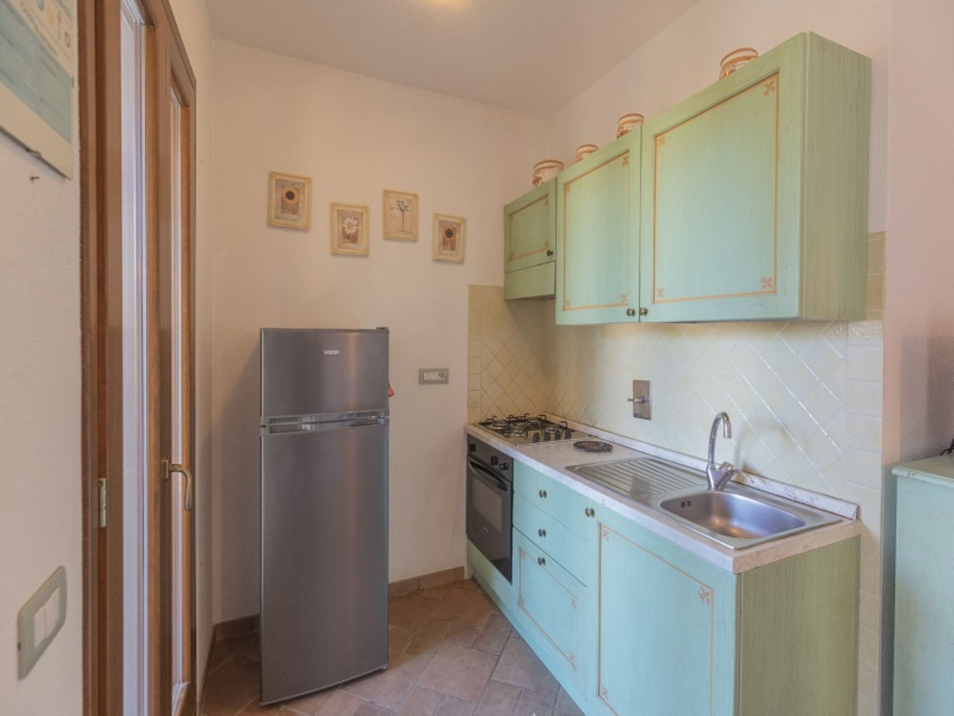 A compact kitchen with a stainless steel refrigerator, a gas stove, and light green cabinets.