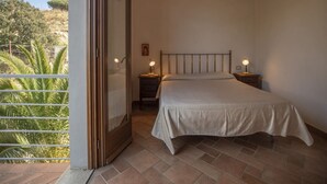 Une chambre à coucher avec un lit, des tables de chevet et un balcon donnant sur un espace verdoyant.