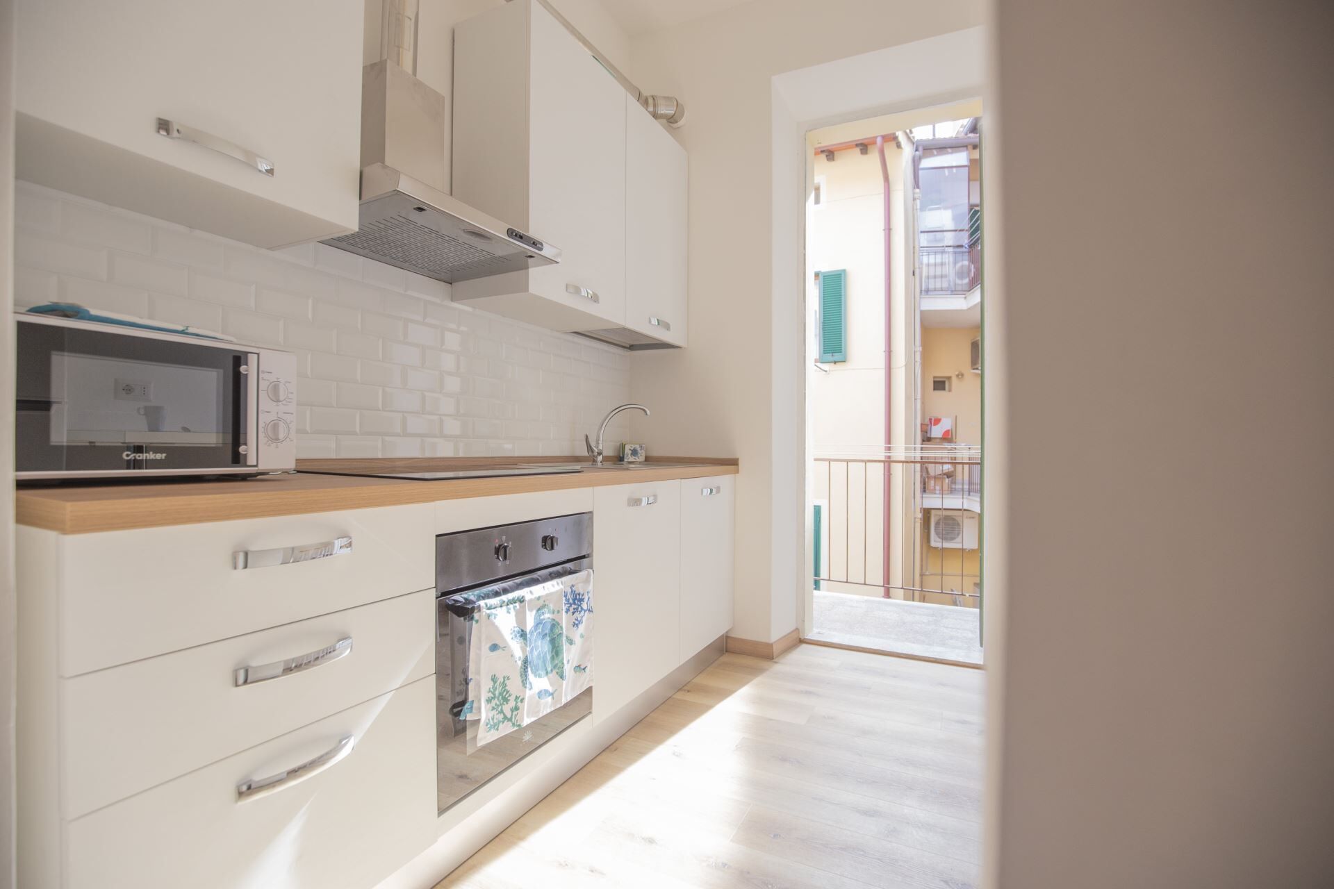 A modern kitchen with white cabinets, a built-in oven, a microwave, and a stainless steel range hood.