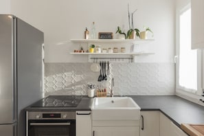 Een moderne keuken met een roestvrijstalen koelkast, een zwart inductiekookplaatje, een witte spoelbak en een backsplash met een herringbone-patroon.