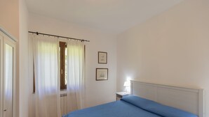 A bedroom with a bed, a window with curtains, a bedside table, and two framed pictures on the wall. - It is located on the ground floor of a building consisting of three terraced houses. ' It consists o (Capoliveri)
