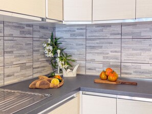 Eine Küche mit grauen Fliesen an der Spritzschutzwand, einem Spülbecken und einer Arbeitsplatte mit Obst und Gemüse.
