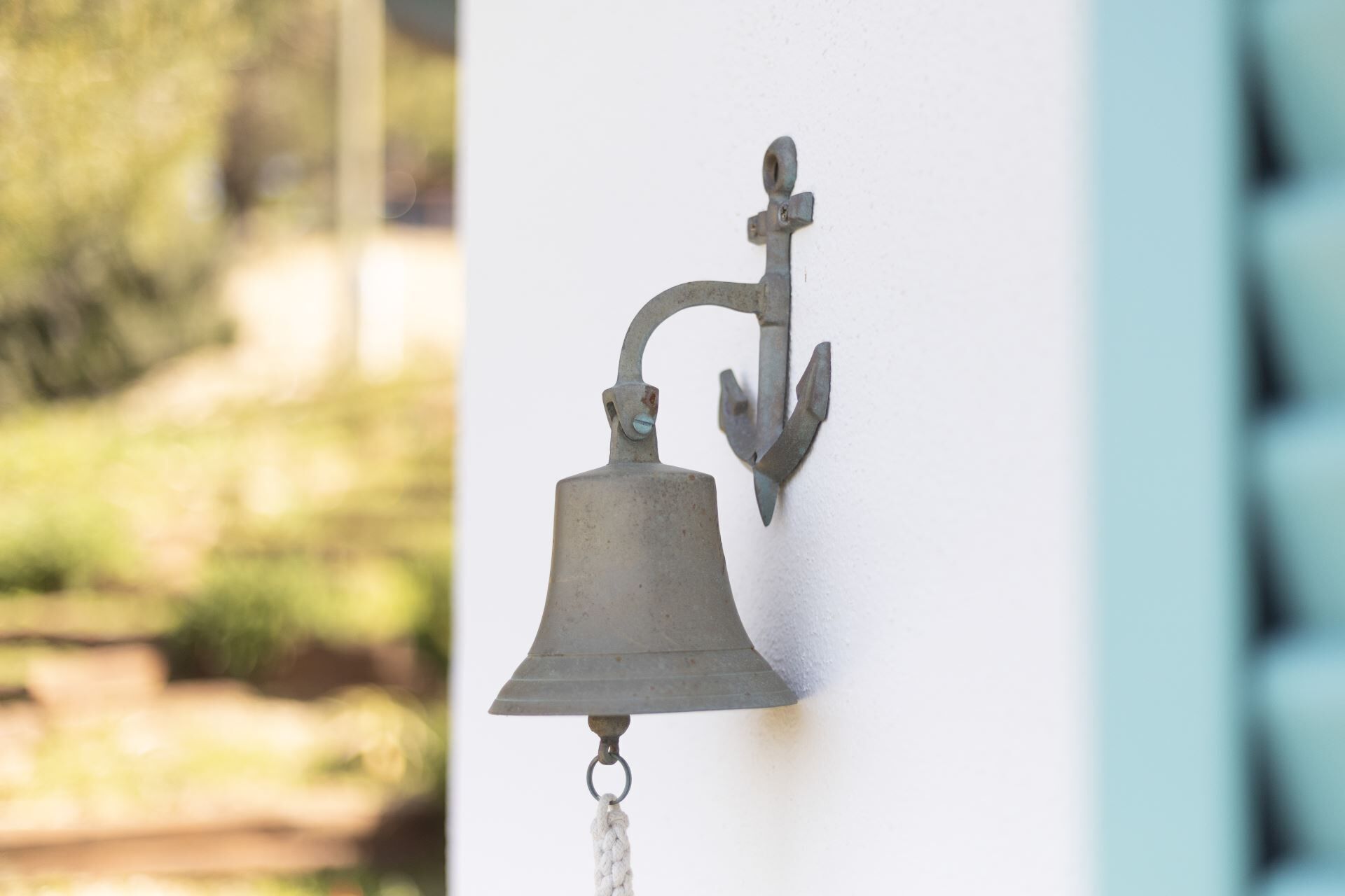 A metal bell mounted on a wall with a rope hanging from it.
