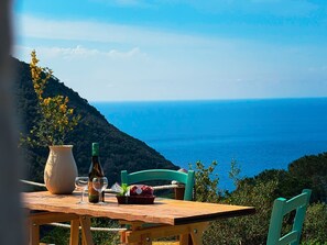 A wooden table with a bottle of wine, glasses, and a basket of food, overlooking a coastal landscape.
