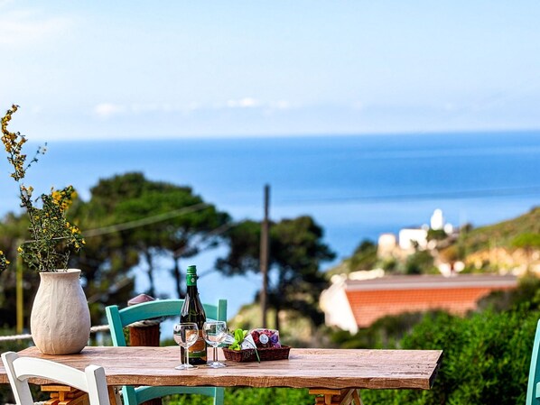 A wooden table with a bottle, glasses, and a basket of fruit.