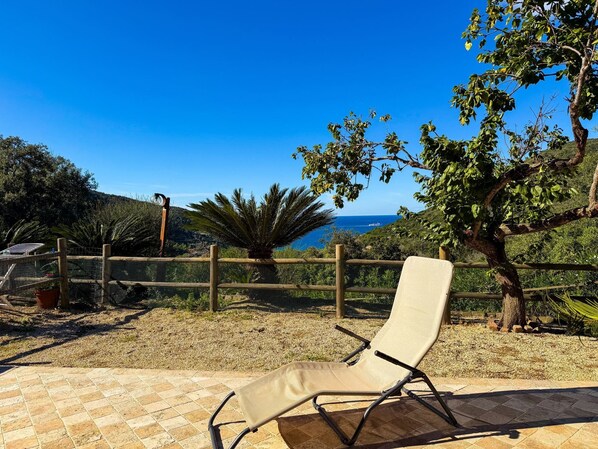 A sun lounger on a tiled patio with a view of the sea and hills.