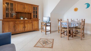 Un coin repas avec une table et des chaises en bois, un téléviseur posé sur un petit meuble, et une grande armoire en bois dotée de portes en verre.