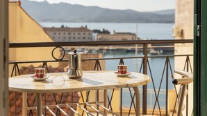En balkon med et bord og stole, med udsigt over vand og bygninger i det fjerne.
