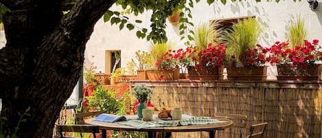 A patio with a table and chairs, surrounded by potted plants and a bamboo fence.