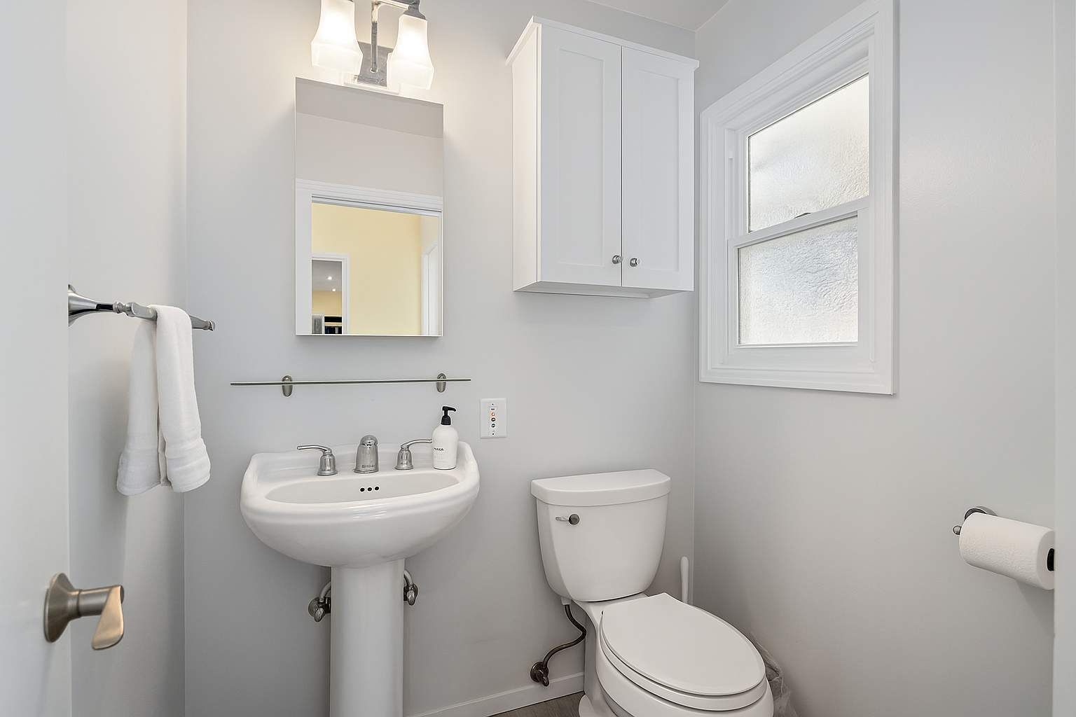 A bathroom with a white sink, a toilet, a mirror, and a window.
